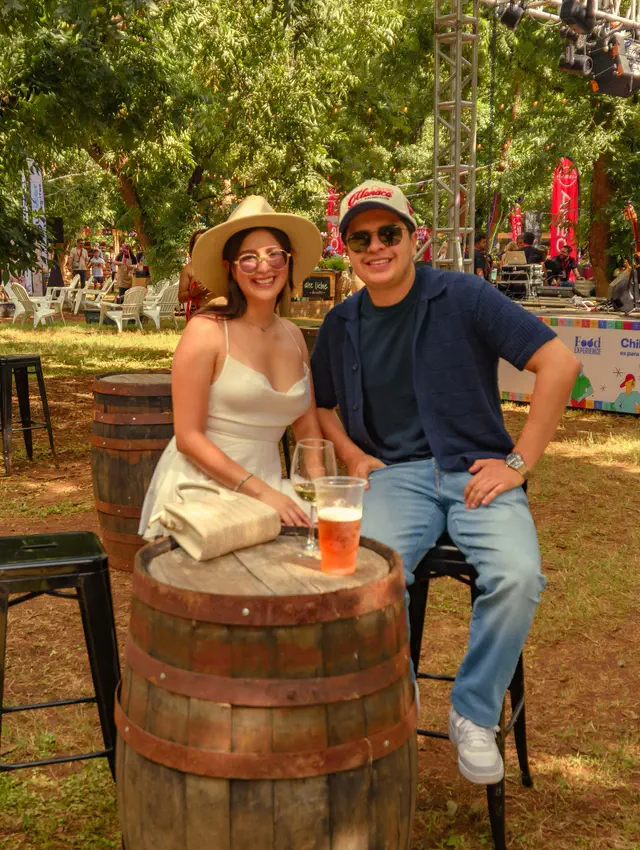 Dos asistentes sentados en una mesa alta hecha con un barril