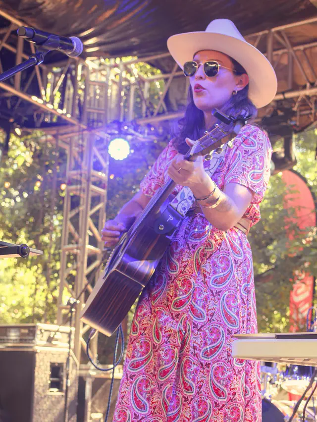 Una música tocando la guitarra en el escenario, entre los árboles