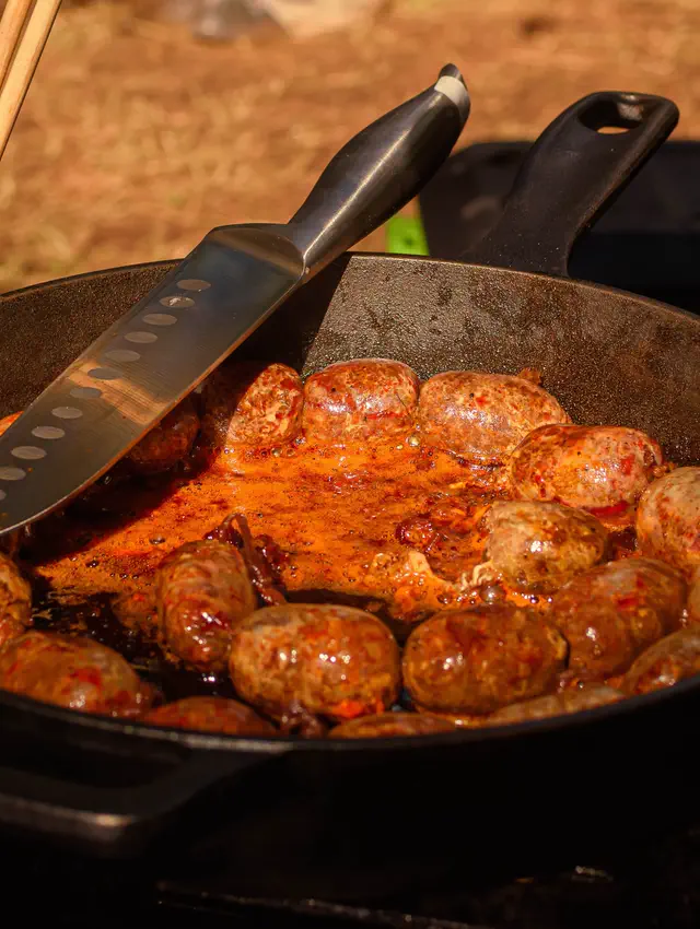 Sartén de hierro con embutidos guisados en salsa, al fuego